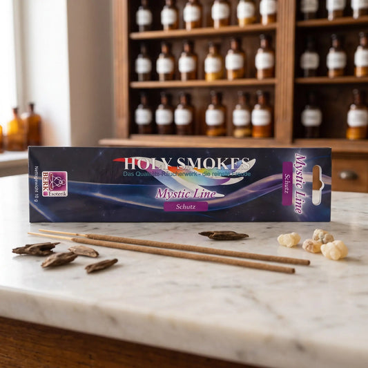 Schutz Räucherstäbchen Holy Smokes Mystic Line: Packung auf einer Marmortheke vor einem Apothekerschrank, davor zwei lose Räucherstäbchen, Adlerholz und Weihrauchharz – Spirit of Gaia