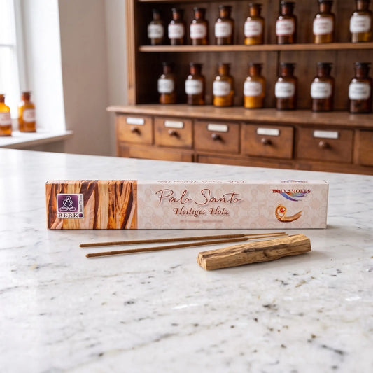 Räucherstäbchen Palo Santo von Berk: Packung auf einer Marmortheke vor einem Apothekerschrank, davor zwei lose Räucherstäbchen und ein Stück Palo-Santo-Holz – Spirit of Gaia