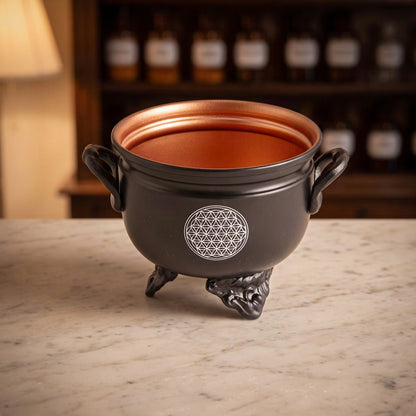 Räuchergefäß Caldron Blume des Lebens von Berk: kleiner schwarzer Eisenkessel mit kupferfarbenem Innenraum und weißem Blume-des-Lebens-Motiv auf der Marmortheke einer Apotheke