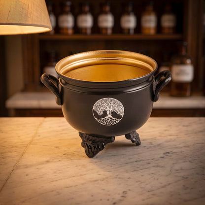 Räuchergefäß Caldron Lebensbaum von Berk: kleiner schwarzer Eisenkessel mit goldfarbenem Innenraum und weißem Lebensbaum-Motiv auf der Marmortheke einer Apotheke