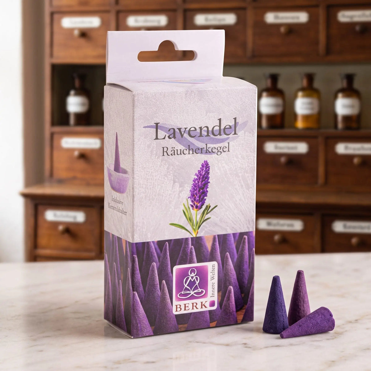 Lavendelblüten Räucherkegel von Berk: Packung auf einer Marmortheke vor einem Apothekerschrank, daneben drei lose violette Räucherkegel – Spirit of Gaia