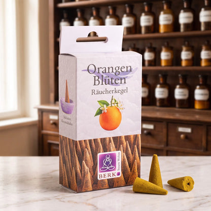 Orangenblüten Räucherkegel von Berk: Packung auf einer Marmortheke vor einem Apothekerschrank, daneben drei lose senfgelbe Räucherkegel – Spirit of Gaia