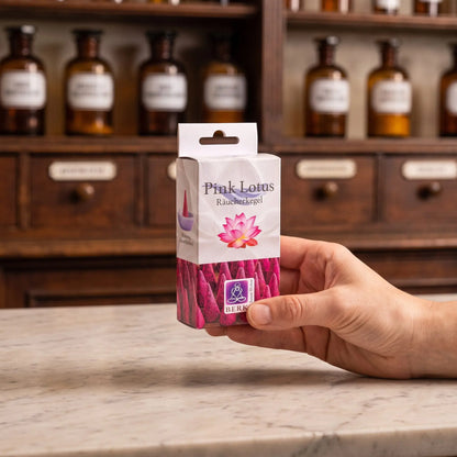 Größenvergleich: eine Hand hält die schmale Packung der Pink Lotus Räucherkegel von Berk vor dem Apothekerschrank