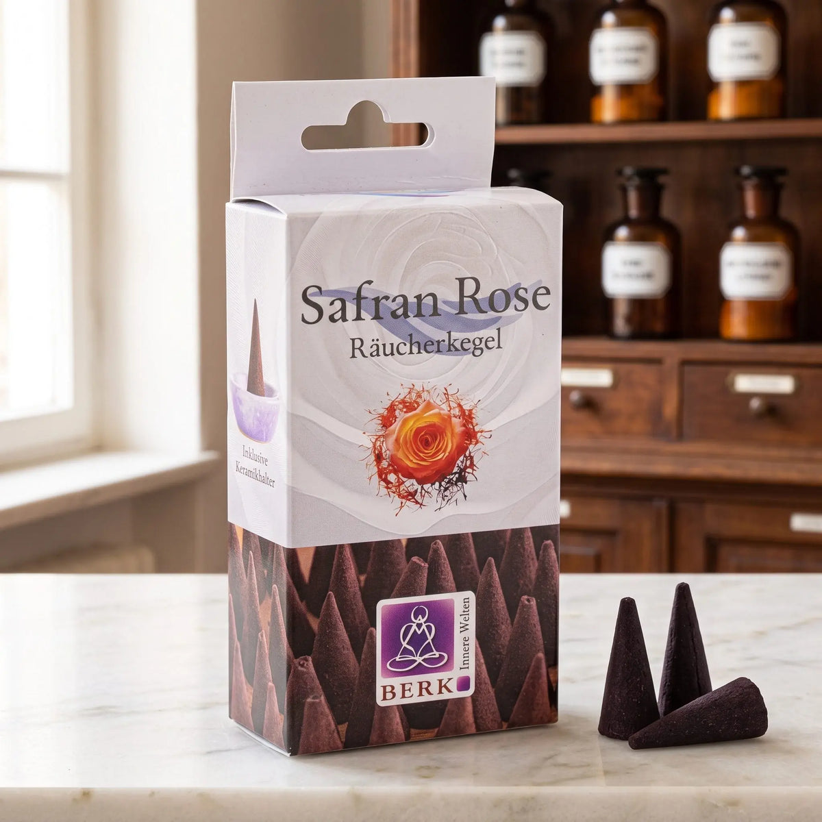 Safran Rose Räucherkegel von Berk: Packung auf einer Marmortheke vor einem Apothekerschrank, daneben drei lose dunkelbraune Räucherkegel – Spirit of Gaia