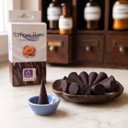 Lieferumfang der Safran Rose Räucherkegel von Berk: dunkelbraune Kegel in einer Holzschale, ein Kegel im beiliegenden blauen Keramikschälchen, dahinter die Packung