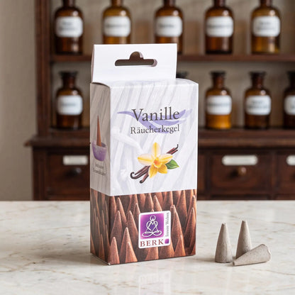 Vanille Räucherkegel von Berk: Packung auf einer Marmortheke vor einem Apothekerschrank, daneben drei lose hellbraune Räucherkegel – Spirit of Gaia