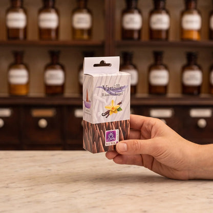 Größenvergleich: eine Hand hält die schmale Packung der Vanille Räucherkegel von Berk vor dem Apothekerschrank