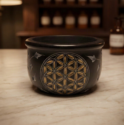 Räucherschale Blume des Lebens von Berk: kleine schwarze Specksteinschale mit goldener Gravur und Blattranken auf der Marmortheke einer Apotheke am Abend