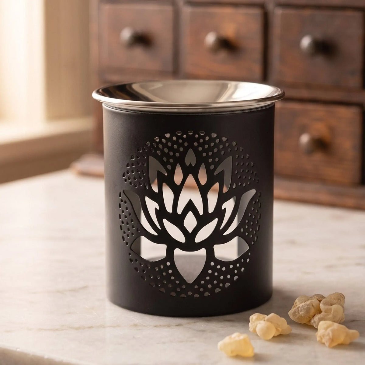 Schwarzes Räuchergefäß aus Eisen mit ausgestanztem Lotus und flacher Edelstahlschale – auf der Marmortheke vor dem Apothekerschrank