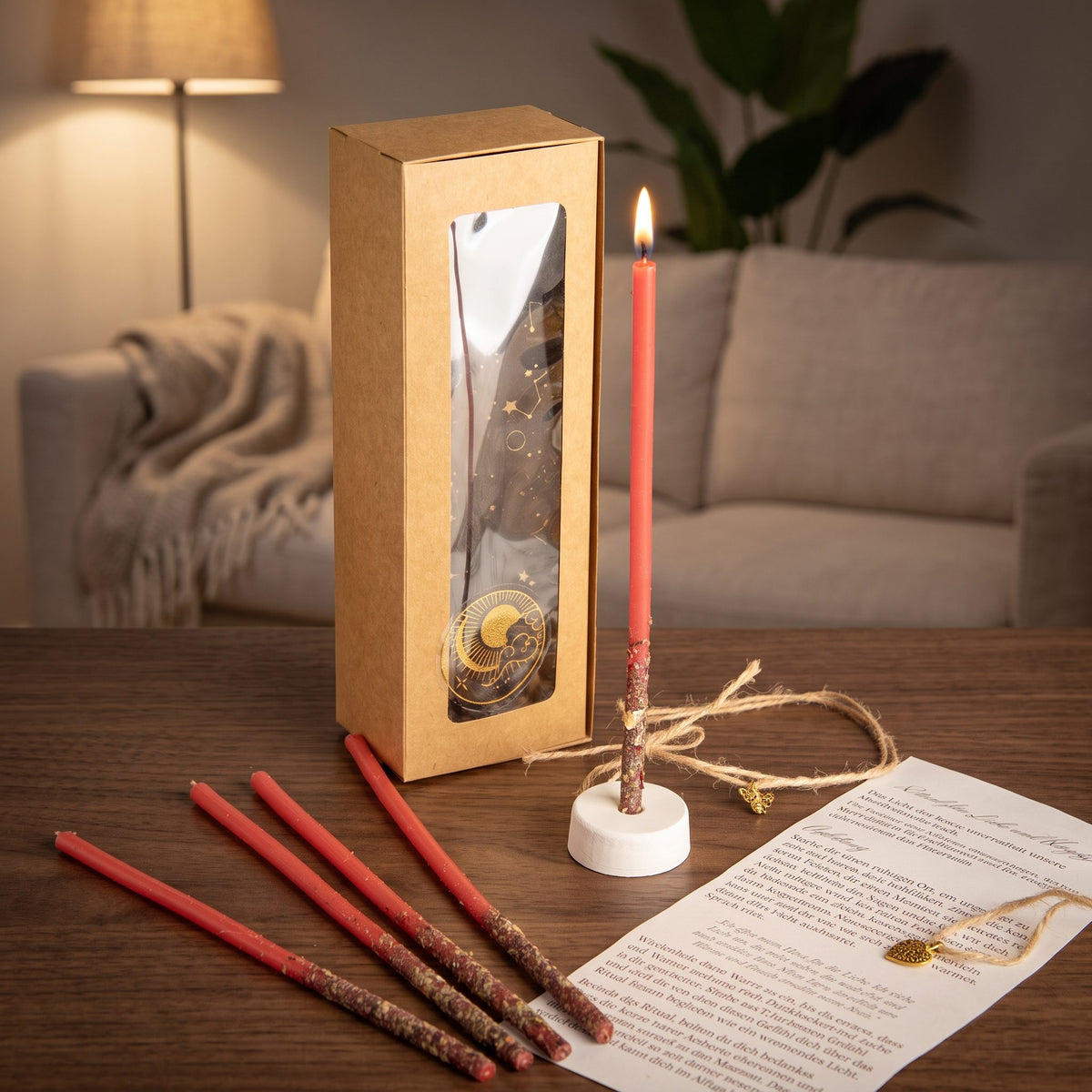Das Set Herzflamme auf einem dunklen Holztisch im Wohnzimmer am Abend, eine Kerze brennt im Ständer, vier weitere liegen davor, dazu die Anleitung und das Amulett