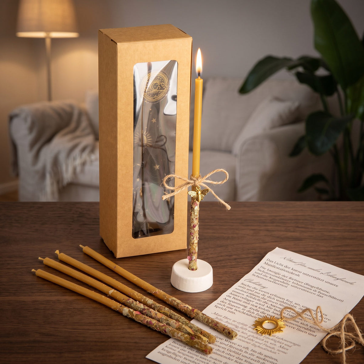 Das Set Lebensfunke auf einem dunklen Holztisch im Wohnzimmer am Abend, eine Kerze brennt im Ständer, vier weitere liegen davor, dazu die Anleitung und das Amulett