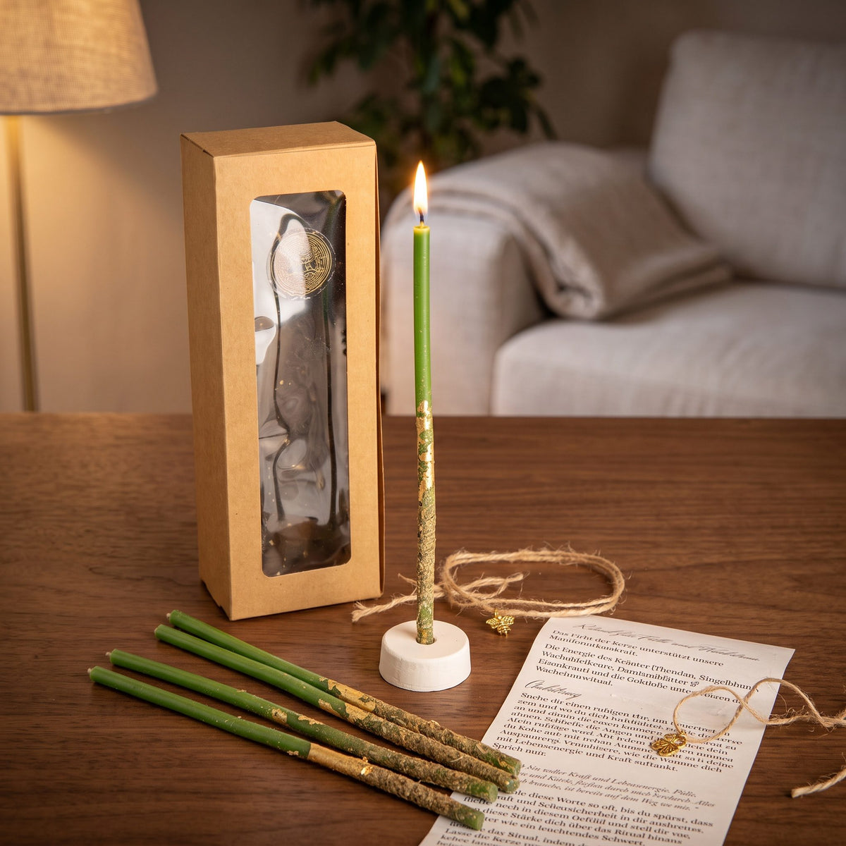 Das Set Wachstumslicht auf einem dunklen Holztisch im Wohnzimmer am Abend, eine Kerze brennt im Ständer, vier weitere liegen davor, dazu die Anleitung und das Amulett