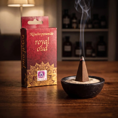 Eine Royal-Oud-Räucherpyramide glimmt auf Sand in einer Specksteinschale, dahinter die Schachtel