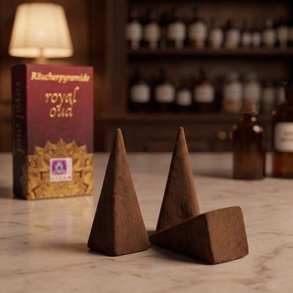 Drei dunkelbraune Royal-Oud-Räucherpyramiden mit vier Kanten aus der Nähe auf einer Marmortheke, dahinter unscharf die rote Schachtel
