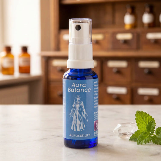 Energiespray Auraschutz (Aura Balance): blaue Sprühflasche mit blauem Etikett auf Marmortheke vor Apothekerschrank, daneben ein Bergkristall und Melissenblätter – Spirit of Gaia