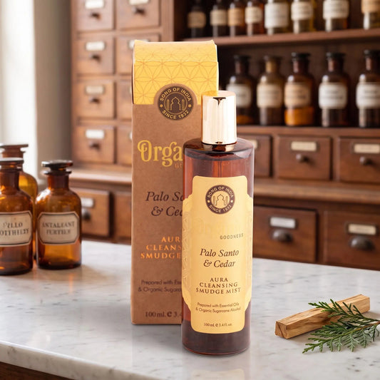 Aura Reinigungsspray Palo Santo und Zeder von Organic Goodness: braune Sprühflasche mit goldener Kappe neben der Kraftpapier-Schachtel auf einer Marmortheke vor einem Apothekerschrank