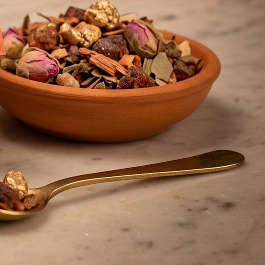 Engel der Fülle, Engelräucherung von Berk, 40 ml im Kugelglas: Nahaufnahme der Terracottaschale mit goldbestäubten Harzen, rotbraunen Stücken und Rosenknospen und dem Messinglöffel auf der Marmortheke – Spirit of Gaia