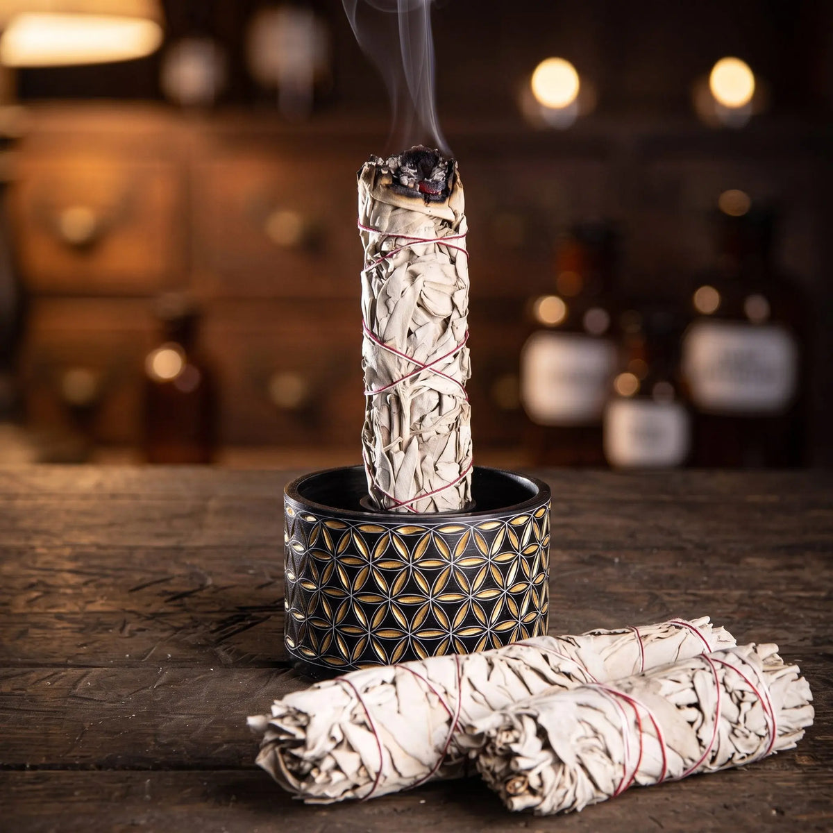 Ein weißes Salbeibündel steht glimmend im Ring der großen schwarz-goldenen Smudge Bowl