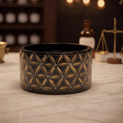 Smudge Bowl Blume des Lebens klein von Berk: schwarze Specksteinschale mit goldener Gravur auf der Marmortheke einer Apotheke am Abend