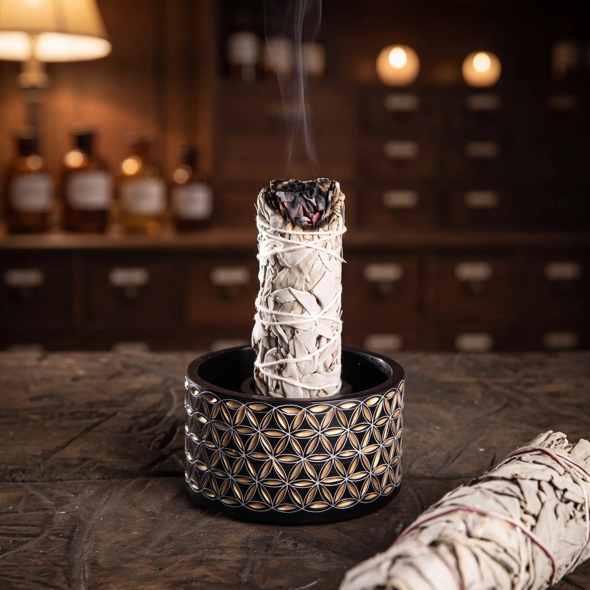 Ein weißes Salbeibündel steht glimmend im Ring der schwarz-goldenen Smudge Bowl