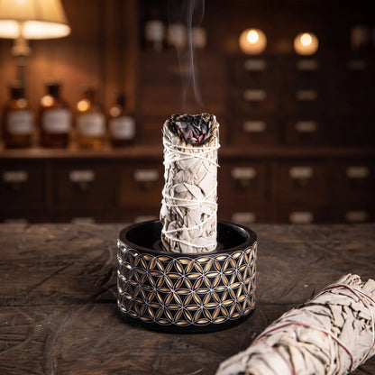 Ein weißes Salbeibündel steht glimmend im Ring der schwarz-goldenen Smudge Bowl