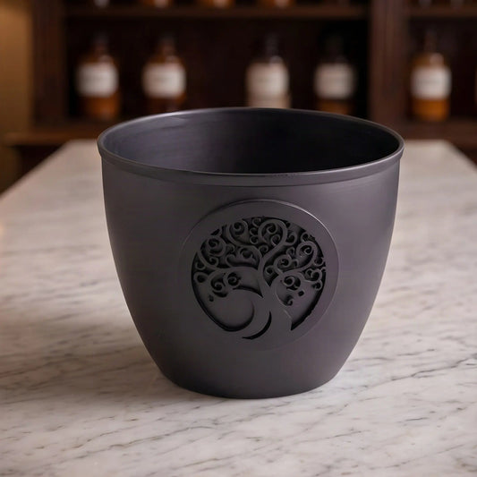 Smudge Bowl Lebensbaum von Berk: große Schale aus mattschwarzem Eisen mit runder Lebensbaum-Scheibe auf der Marmortheke einer Apotheke am Abend