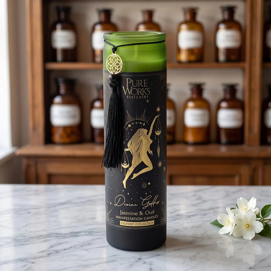 Manifestationskerze Divine Goddess (Jasmin & Oud) von Pure Works: hohe Glaskerze mit grünem Glasrand, schwarzer Quaste und Goldanhänger auf Marmortheke vor Apothekerschrank, daneben weiße Jasminblüten – Spirit of Gaia