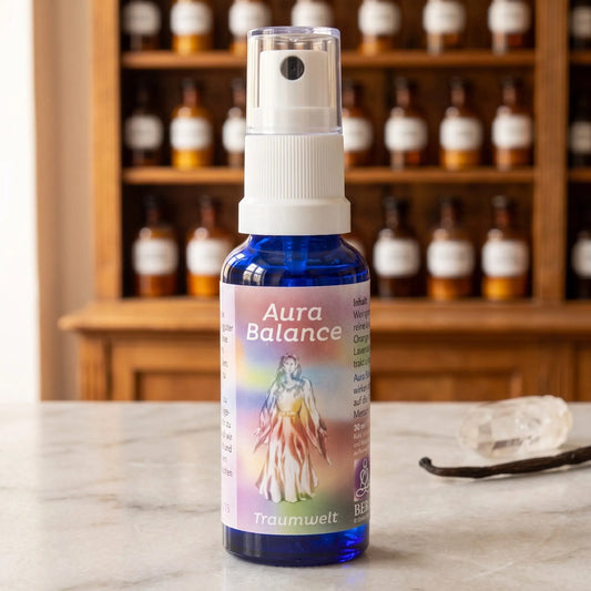Energiespray Traumwelt (Aura Balance): blaue Sprühflasche mit regenbogenfarbenem Etikett auf Marmortheke vor Apothekerschrank, daneben ein Bergkristall und eine Vanilleschote – Spirit of Gaia