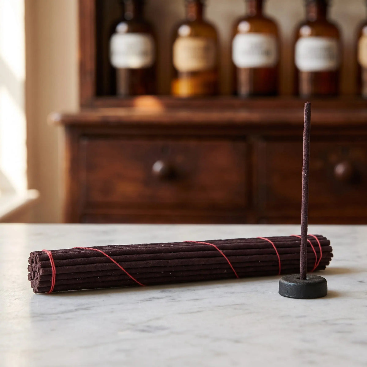 Lieferumfang der tibetischen Räucherstäbchen Dolma Incense von Berk: das Stäbchenbündel mit roter Schnur und die flache Tonscheibe als Halter auf der Marmortheke