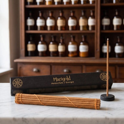 Tibetische Räucherstäbchen Marigold von Berk: schwarze Schachtel mit Goldschrift auf einer Marmortheke vor einem Apothekerschrank, davor das Stäbchenbündel und der Tonhalter