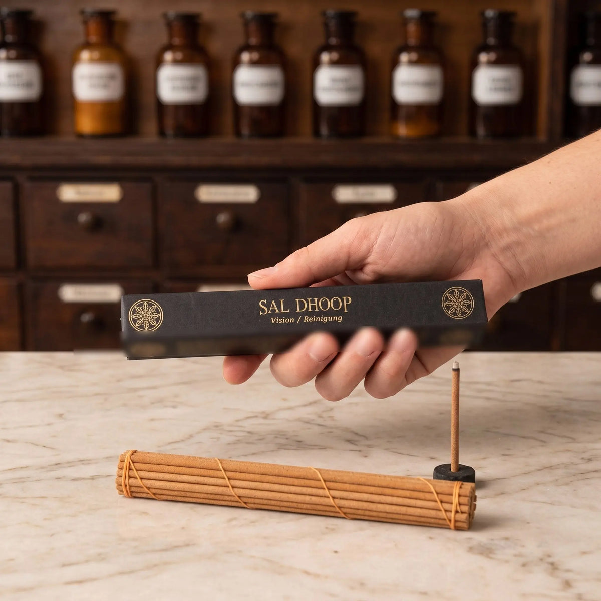 Größenvergleich: eine Hand hält die längliche Schachtel der tibetischen Räucherstäbchen Sal Dhoop von Berk