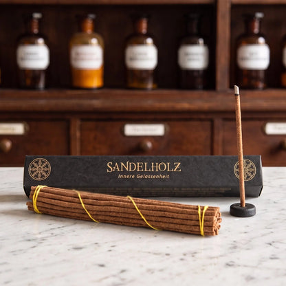 Tibetische Räucherstäbchen Sandelholz von Berk: schwarze Schachtel mit Goldschrift auf einer Marmortheke vor einem Apothekerschrank, davor das Stäbchenbündel und der Tonhalter – Spirit of Gaia