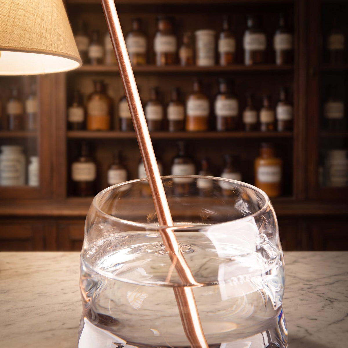 Trinkhalm aus Kupfer in einem Glas Wasser auf einer Apothekentheke am Abend