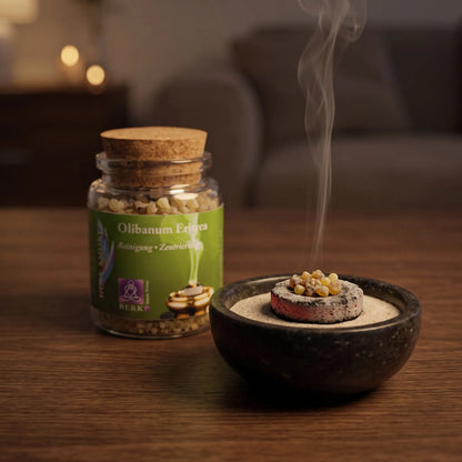 Olibanum Eritrea, reiner Weihrauch von Berk, 60 ml im Korkglas: einige kleine Weihrauchkörner glimmen auf der Räucherkohle, dahinter das Korkglas, feiner Rauch steigt auf einer dunklen Holzplatte am Abend auf – Spirit of Gaia