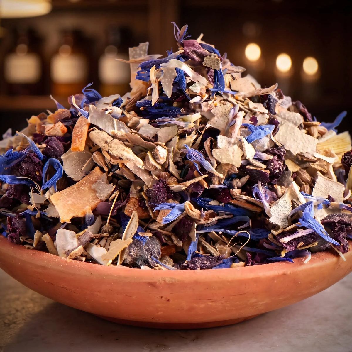 Klarträume, Räuchermischung der Reihe Kraftvoll Räuchern von Berk, 60 ml im Bügelglas: Nahaufnahme der Terracottaschale mit blauen Kornblumen und hellen Holzspänen vor der warmen, unscharfen Abendapotheke – Spirit of Gaia