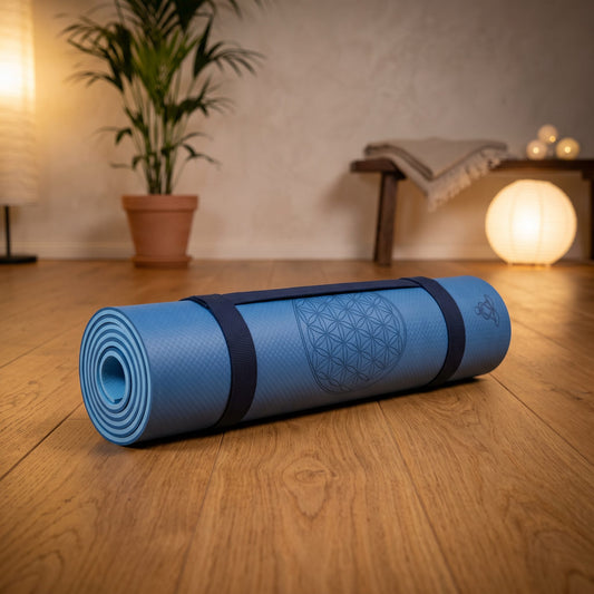 EcoBalance Yogamatte aus TPE, 182 × 61 cm, 6 mm, Blume des Lebens, dunkel-/hellblau: eingerollt mit Tragegurt auf dem Holzboden eines ruhigen Meditationsraums am Abend – Spirit of Gaia