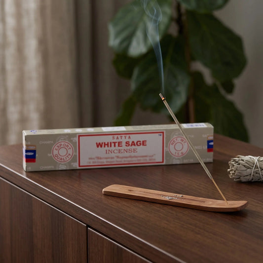 Satya White Sage Räucherstäbchen: glimmendes Räucherstäbchen mit feinem Rauch im Holzhalter, dahinter die Packung, auf einem Sideboard am Abend