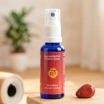 Ayurvedisches Chakra-Spray Muladhara (Wurzel-Chakra): 30-ml-Sprühflasche auf einem Holzhocker neben einer gerollten Yogamatte, daneben roter Jaspis