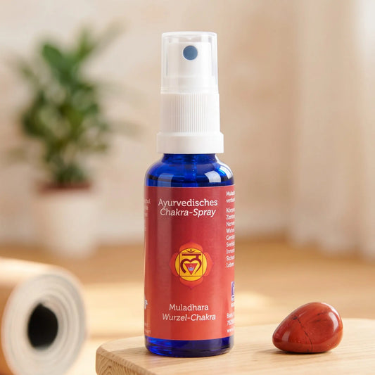 Ayurvedisches Chakra-Spray Muladhara (Wurzel-Chakra): 30-ml-Sprühflasche auf einem Holzhocker neben einer gerollten Yogamatte, daneben roter Jaspis