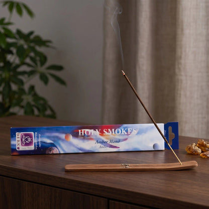 Amber Mond Räucherstäbchen Holy Smokes Blue Line: glimmendes Räucherstäbchen mit feinem Rauch im Holzhalter, dahinter die Packung, auf einem Sideboard am Abend