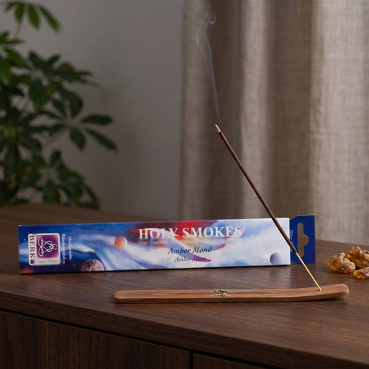 Amber Mond Räucherstäbchen Holy Smokes Blue Line: glimmendes Räucherstäbchen mit feinem Rauch im Holzhalter, dahinter die Packung, auf einem Sideboard am Abend