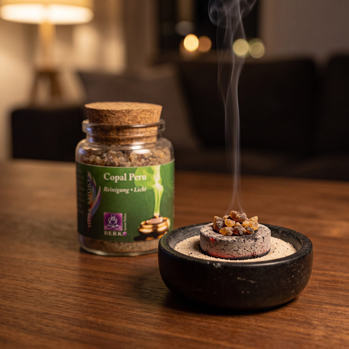 Copal Peru, reines Räucherharz von Berk, 60 ml im Korkglas: glimmende Räucherkohle mit einigen Copalstücken in einer Specksteinschale, dahinter das Korkglas, feiner Rauch steigt auf einer dunklen Holzplatte am Abend auf – Spirit of Gaia