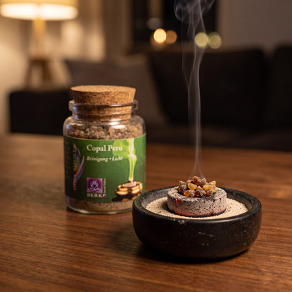 Copal Peru, reines Räucherharz von Berk, 60 ml im Korkglas: glimmende Räucherkohle mit einigen Copalstücken in einer Specksteinschale, dahinter das Korkglas, feiner Rauch steigt auf einer dunklen Holzplatte am Abend auf – Spirit of Gaia