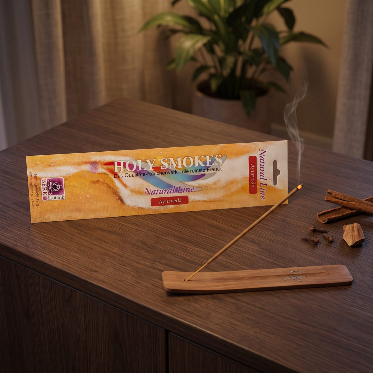 Ayurveda Räucherstäbchen Natural Line: glimmendes Stäbchen im Holzhalter auf einem dunklen Sideboard, dahinter die Packung, am Abend