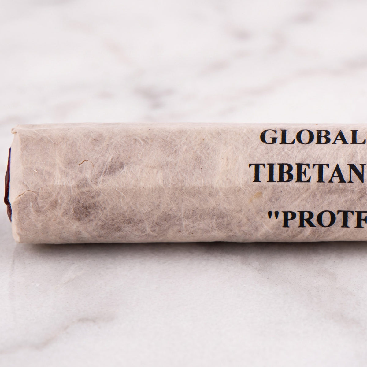 Nahaufnahme der Papierrolle Schutz (Protection) mit der Aufschrift Global Shaman Tibetan Incense und den roten Stäbchenenden auf Marmor