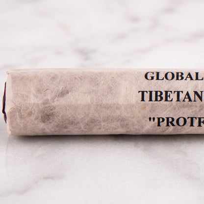 Nahaufnahme der Papierrolle Schutz (Protection) mit der Aufschrift Global Shaman Tibetan Incense und den roten Stäbchenenden auf Marmor