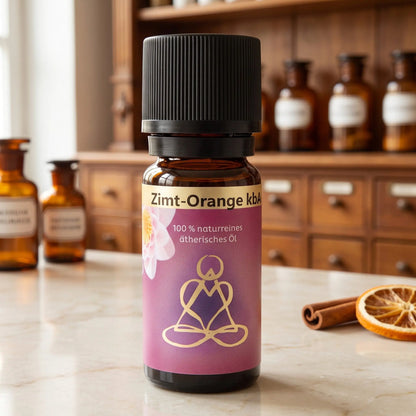 Ätherisches Öl Zimt-Orange: Fläschchen aus Braunglas auf Marmortheke vor Apothekerschrank, daneben eine Zimtstange und eine Orangenscheibe – Spirit of Gaia