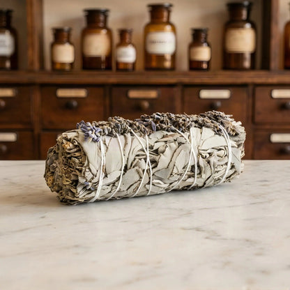 Weißes Salbeibündel mit Lavendelblüten auf Marmorablage vor einem Apothekerschrank – Spirit of Gaia