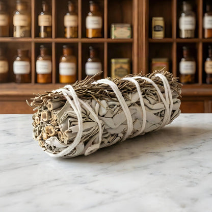 Weißes Salbeibündel mit Rosmarin auf Marmorablage vor einem Apothekerschrank – Spirit of Gaia