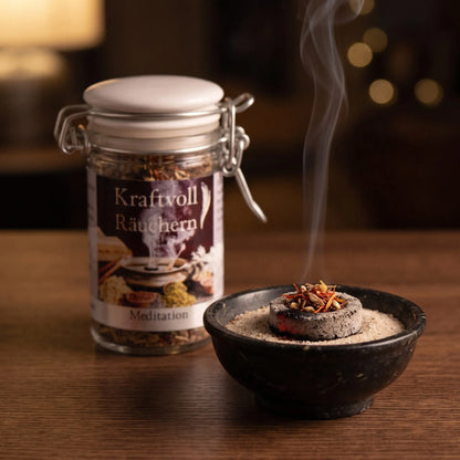 Meditation, Räuchermischung der Reihe Kraftvoll Räuchern von Berk, 60 ml im Bügelglas: eine Prise der Mischung glimmt auf der Räucherkohle, dahinter das Bügelglas, feiner Rauch steigt auf einer dunklen Holzplatte am Abend auf – Spirit of Gaia